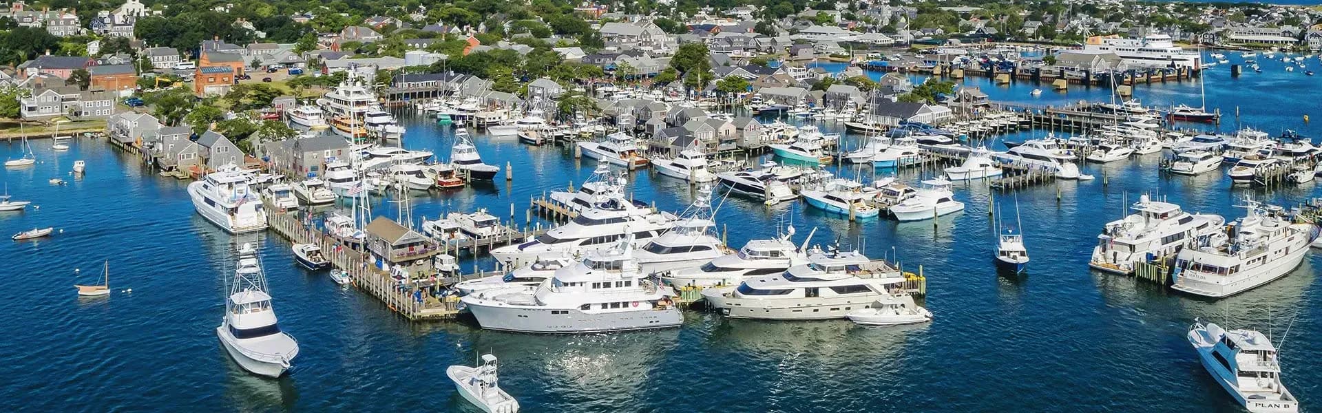 A busy marina seen from above, sportfishing boats and motor yachts lying along the docks below a shingled town